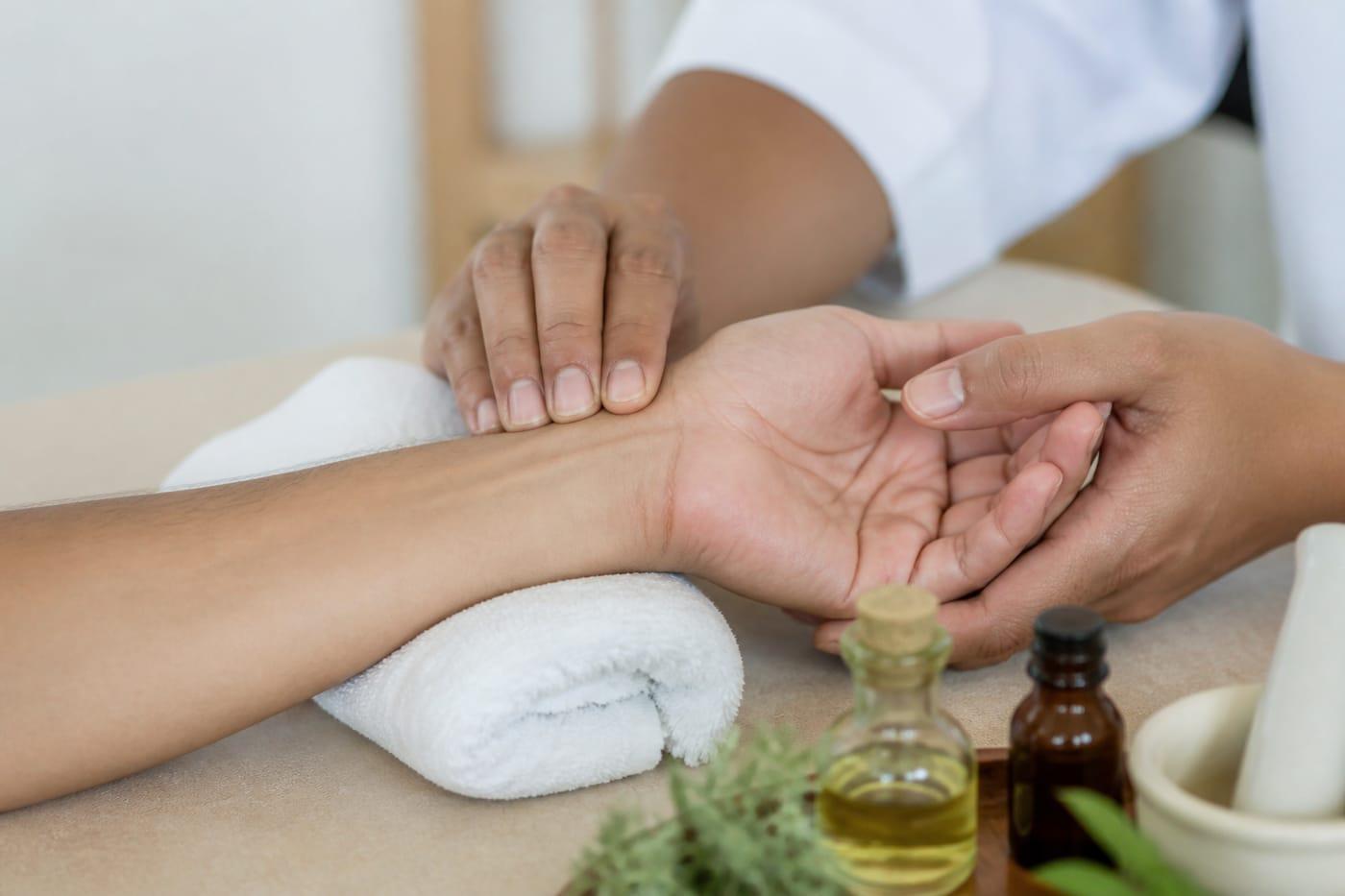 Clinician checking pulse with herbal oils nearby, no faces shown