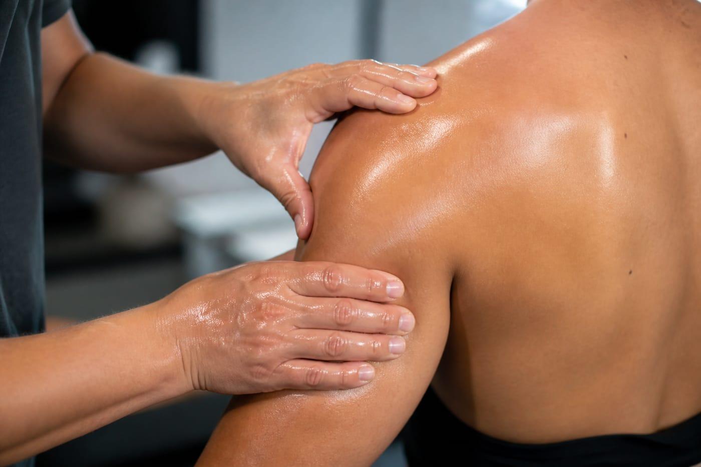 Therapist hands applying warm oil to shoulder and arm, no faces shown