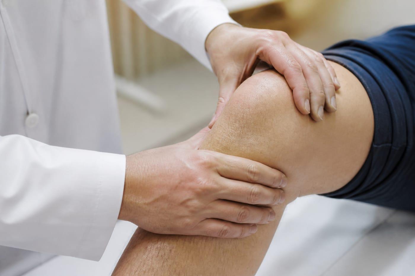 Clinician hands examining a knee joint for rheumatology care, no faces shown